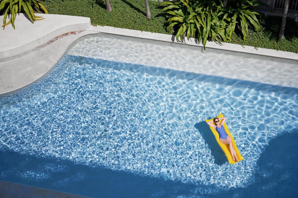 Enjoying suntan. Tropical vacation concept. Top view of young woman on the yellow air mattress in the swimming pool.