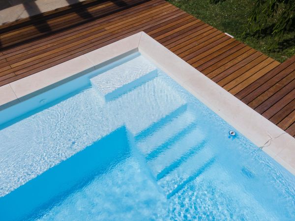 Drone flight over pool with nice wooden terrace surrounded by green lawn in beautiful garden