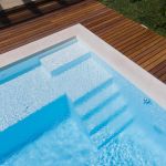 Drone flight over pool with nice wooden terrace surrounded by green lawn in beautiful garden