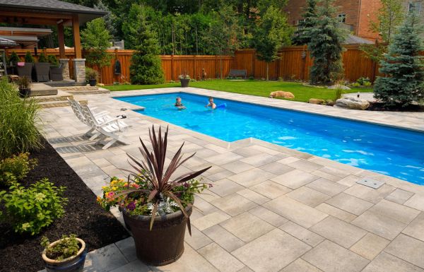 Mother and daughter swimming in new back yard pool with dog a patio of pavers and green lawn and gardens