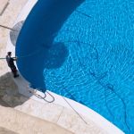 Cleaning and maintenance of swimming pool. Aerial view to maintenance person cleaning swimming pool in sunny day.
