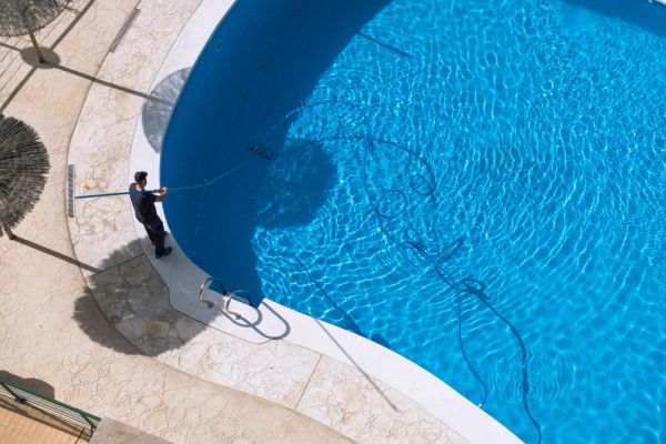 Cleaning and maintenance of swimming pool. Aerial view to maintenance person cleaning swimming pool in sunny day.