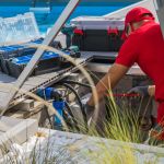 Closeup of Caucasian Professional Worker in Red Uniform Fixing Outdoor Swimming Pool Heating System Using Different Tools. Side View.