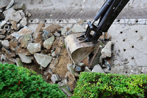 Excavator breaks and removes old concrete sidewalk. Sidewalk reconstruction